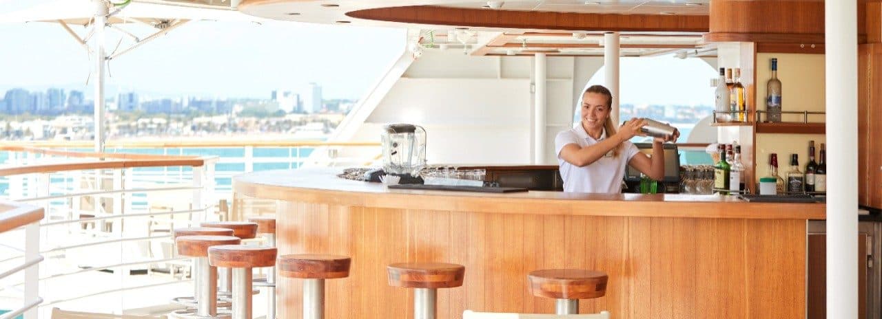 Smiling bartender using shaker behind the Sky Bar aboard an all-inclusive, luxury Seabourn cruise.
